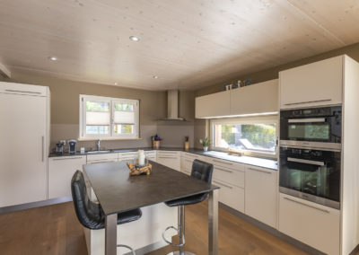 Cette image représente l'intérieur de la cuisine d'une maison individuelle construite en ossature bois par Volery Frères SA. Les planchers sont réalisés grâce à la pose d'une dalle bois visible en plafond et blanchie.