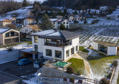 Cette image représente l'extérieur d'une maison individuelle construite en ossature bois réalisée par Volery Frères SA. La couverture de la toiture à aussi été réalisée par l'entreprise. Les fenêtres en bois métal sont produites dans les locaux de l'entreprise à Aumont avant d'être posée sur le chantier.