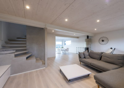 Cette image représente l'intérieur du séjour d'une maison individuelle construite en ossature bois par Volery Frères SA. Les planchers sont réalisés grâce à la pose d'une dalle bois visible en plafond et blanchie. L'escalier est également réalisé par Volery Frères SA et se marie dans les mêmes tons que les plafond et les sols.